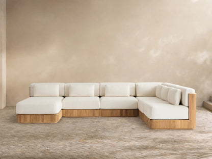 L-shaped Beaumont Teak Sectional with chaise, cream cushions, ribbed golden-brown teak base, on a paved patio.