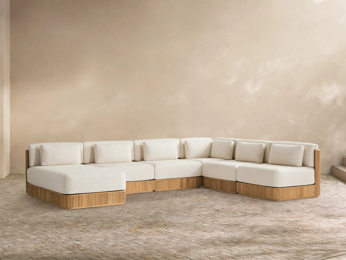 L-shaped Beaumont Teak Sectional with chaise, cream cushions, ribbed golden-brown teak base, on a paved patio.