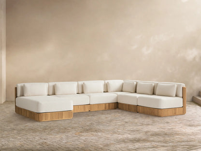 L-shaped Beaumont Teak Sectional with chaise, cream cushions, ribbed golden-brown teak base, on a paved patio.