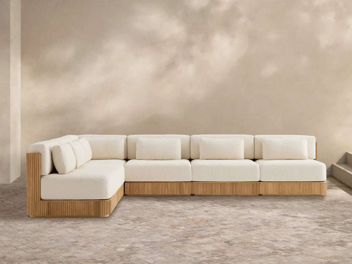 L-shaped Beaumont Outdoor Teak Six-Piece Sectional with grooved teak base & cream cushions on a tiled patio.