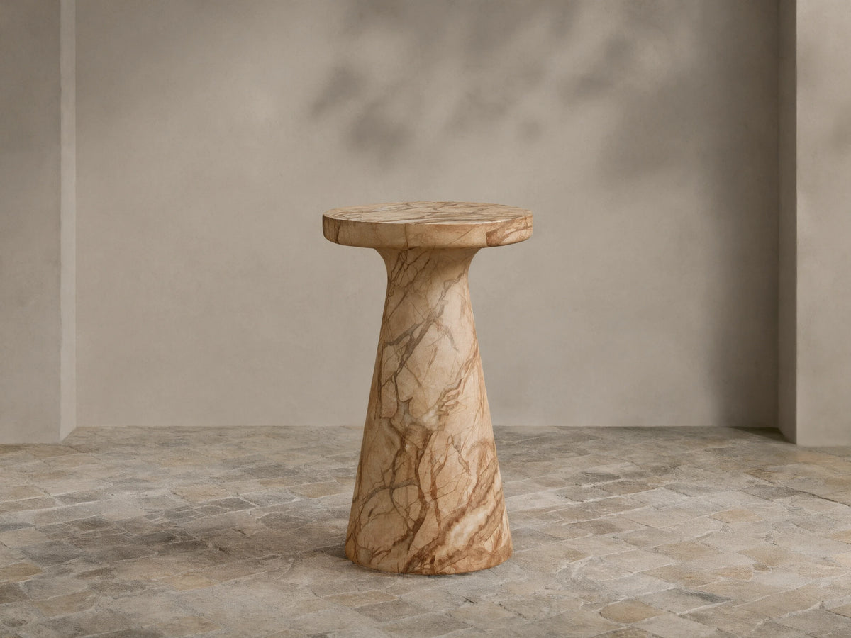 Fira Outdoor End Table: round top, conical base, light brown marble-like finish with dark veining, on stone tiles.