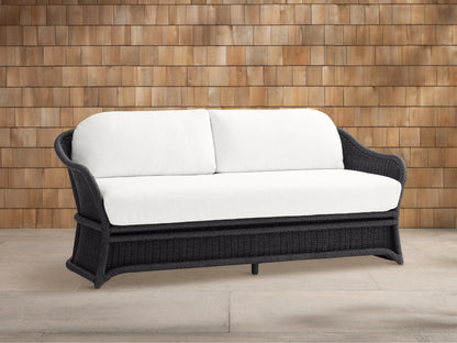 Fowler Outdoor Sofa: Dark gray woven frame with two plush white cushions, set on a concrete patio in front of a wood shingle wall.