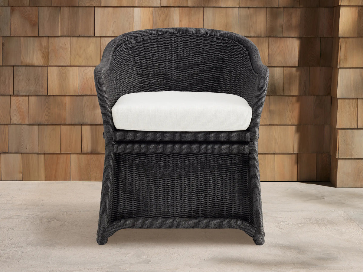 Fowler Outdoor Dining Chair, dark gray handwoven wicker, white cushion, angled right on concrete patio near wood wall.