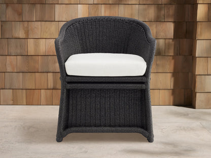 Fowler Outdoor Dining Chair, dark gray handwoven wicker, white cushion, angled right on concrete patio near wood wall.