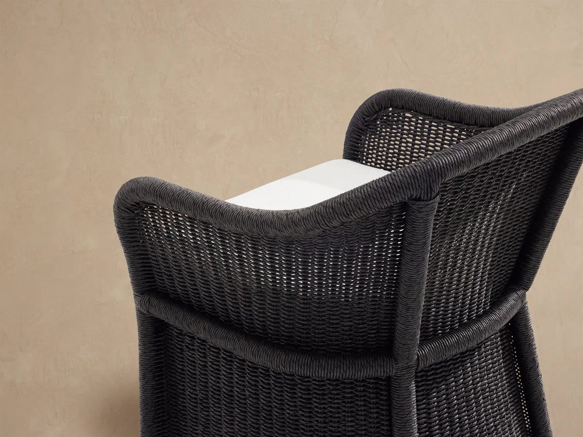 Fowler Outdoor Dining Chair, dark gray handwoven wicker with a rounded back and thick off-white seat cushion.
