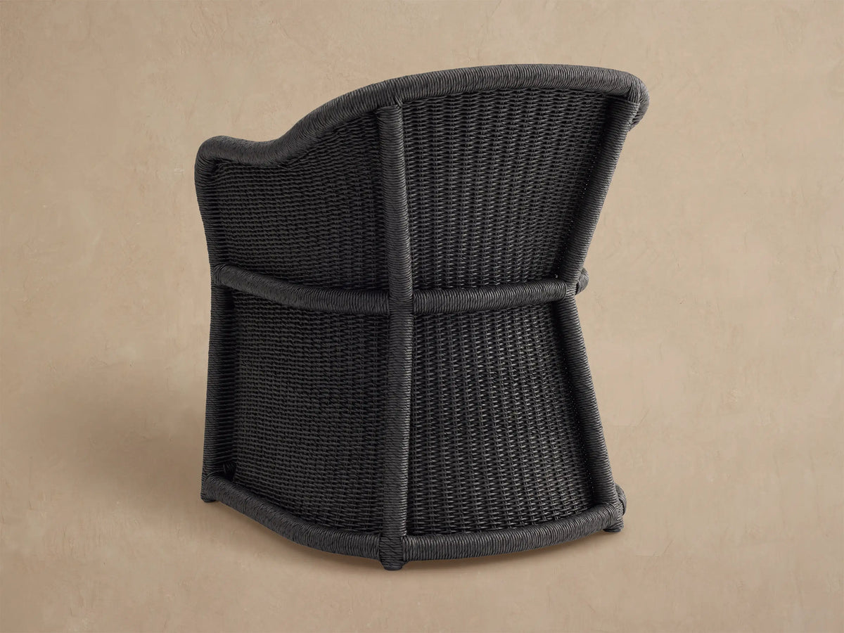 Fowler Outdoor Dining Chair, black handwoven all-weather wicker with white seat cushion, seen from the back-side.