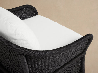 Fowler Outdoor Lounge Chair: dark gray woven all-weather wicker, with thick white seat and back cushions, on a patio.