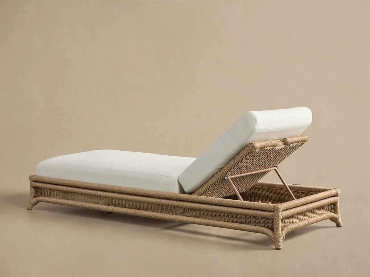 Fowler Outdoor Chaise with raised backrest, showing light brown woven wicker frame, cream cushion, and metal adjustment bar.
