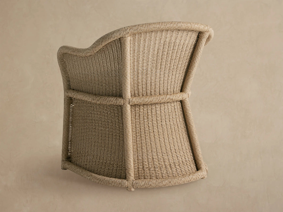 Close-up of Fowler Outdoor Dining Chair, natural woven wicker with braided trim, and a white, textured seat cushion.