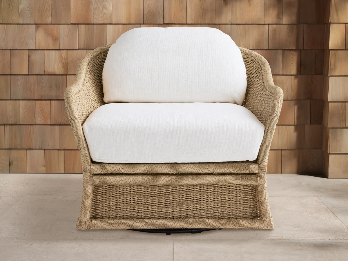 Fowler Outdoor Glider, light brown woven wicker chair with white cushions, angled on light patio tiles against a wood-paneled wall.