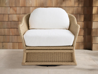 Fowler Outdoor Glider, light brown woven wicker chair with white cushions, angled on light patio tiles against a wood-paneled wall.