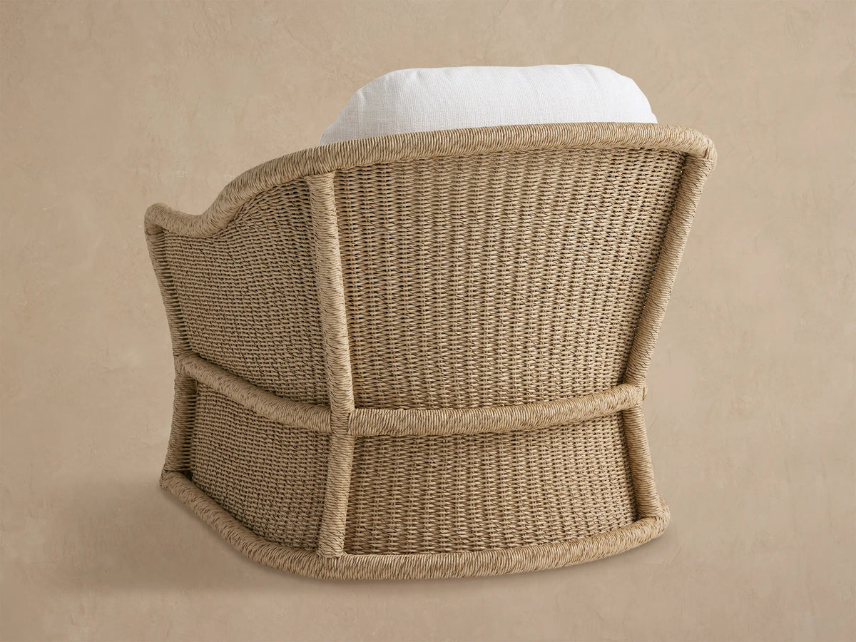Angled view of a Fowler Outdoor Glider, featuring light beige handwoven wicker with thick rounded edges and white cushions.