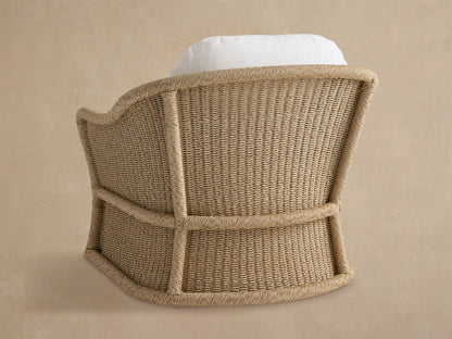 Angled view of a Fowler Outdoor Glider, featuring light beige handwoven wicker with thick rounded edges and white cushions.