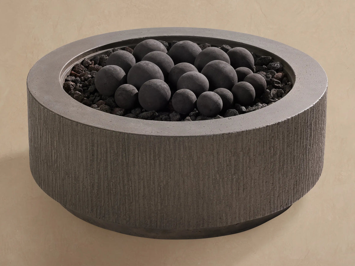 Black outdoor fire pit spheres, various sizes, on dark lava rocks in a textured grey concrete fire pit.