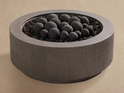 Black outdoor fire pit spheres, various sizes, on dark lava rocks in a textured grey concrete fire pit.