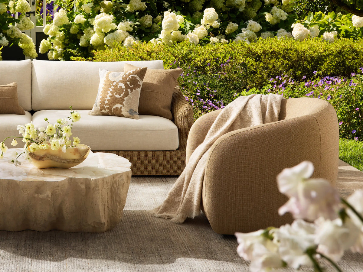 Side view of a tan Fresno Outdoor Swivel Chair, featuring its gracefully curved silhouette and visible woven fabric.
