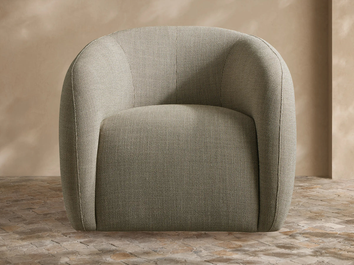 Tan Fresno Outdoor Swivel Chair with curved upholstered back and a light beige throw blanket in an outdoor patio.
