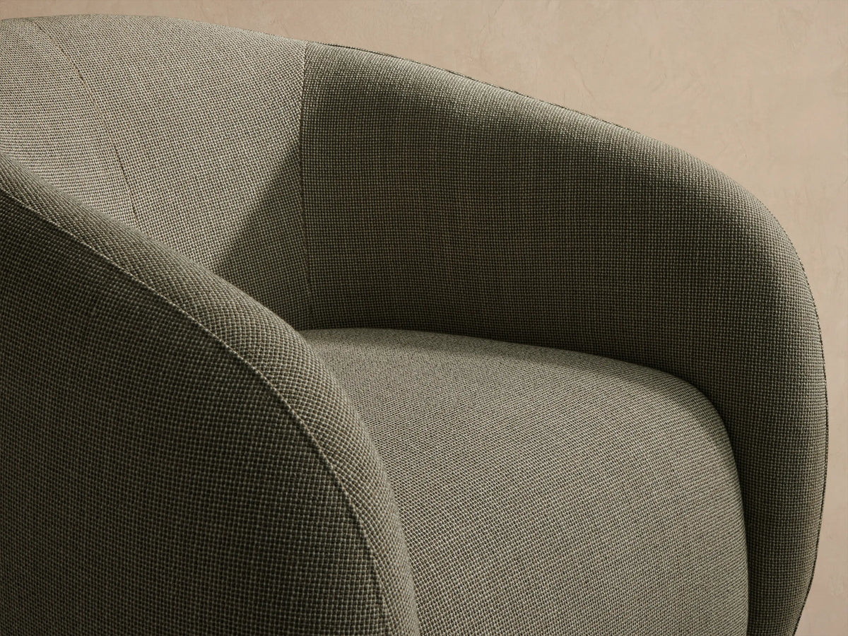 Fresno Outdoor Swivel Chair, rounded barrel-style, light greenish-grey woven upholstery, on patio tiles against a beige wall.