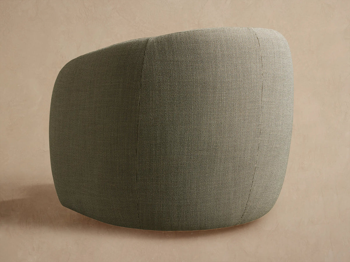 Close-up of Fresno Outdoor Swivel Chair. Dark olive-grey speckled fabric on curved back and armrest, against a light wall.