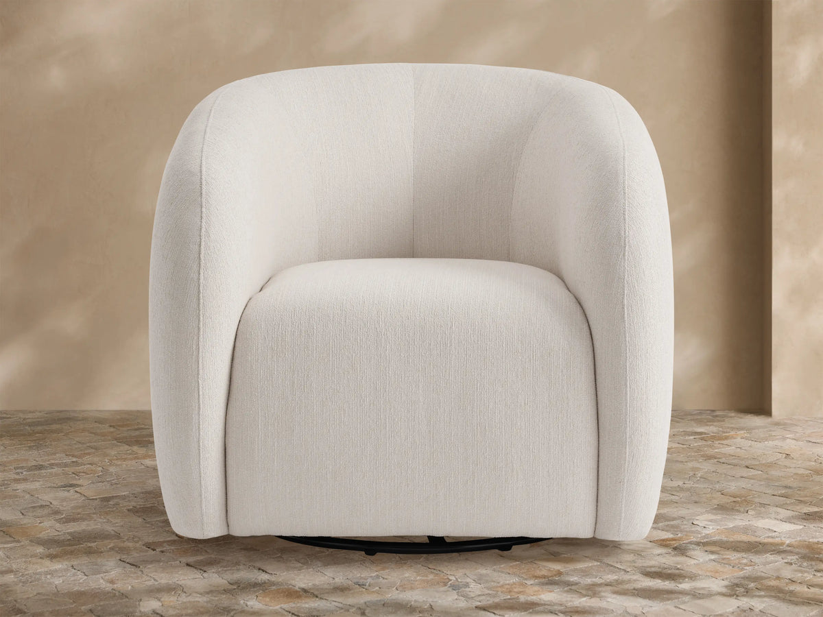 Frontal view of the rounded light brown Fresno Outdoor Swivel Chair, upholstered, with a beige throw blanket, in a lush patio setting.