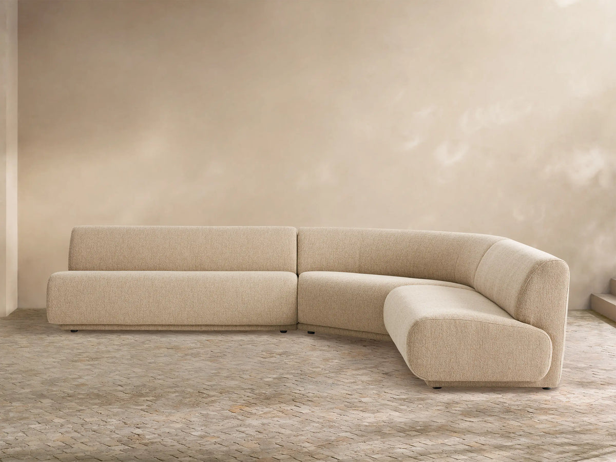 Gianni Outdoor Sectional: Sand-colored, L-shaped sofa with curved armless section, on a light tiled floor against a neutral wall.