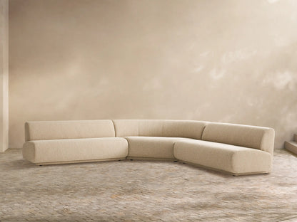 Gianni Outdoor Sectional: Sand-colored, L-shaped sofa with curved armless section, on a light tiled floor against a neutral wall.