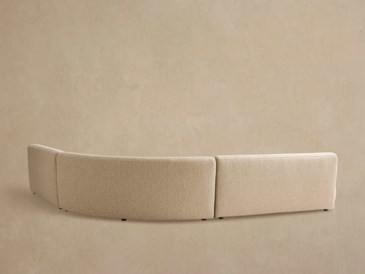 Angled close-up of a curved, beige Gianni Outdoor Sectional. Rounded, plush seat and back cushions feature textured fabric.