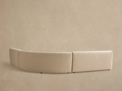 Angled close-up of a curved, beige Gianni Outdoor Sectional. Rounded, plush seat and back cushions feature textured fabric.