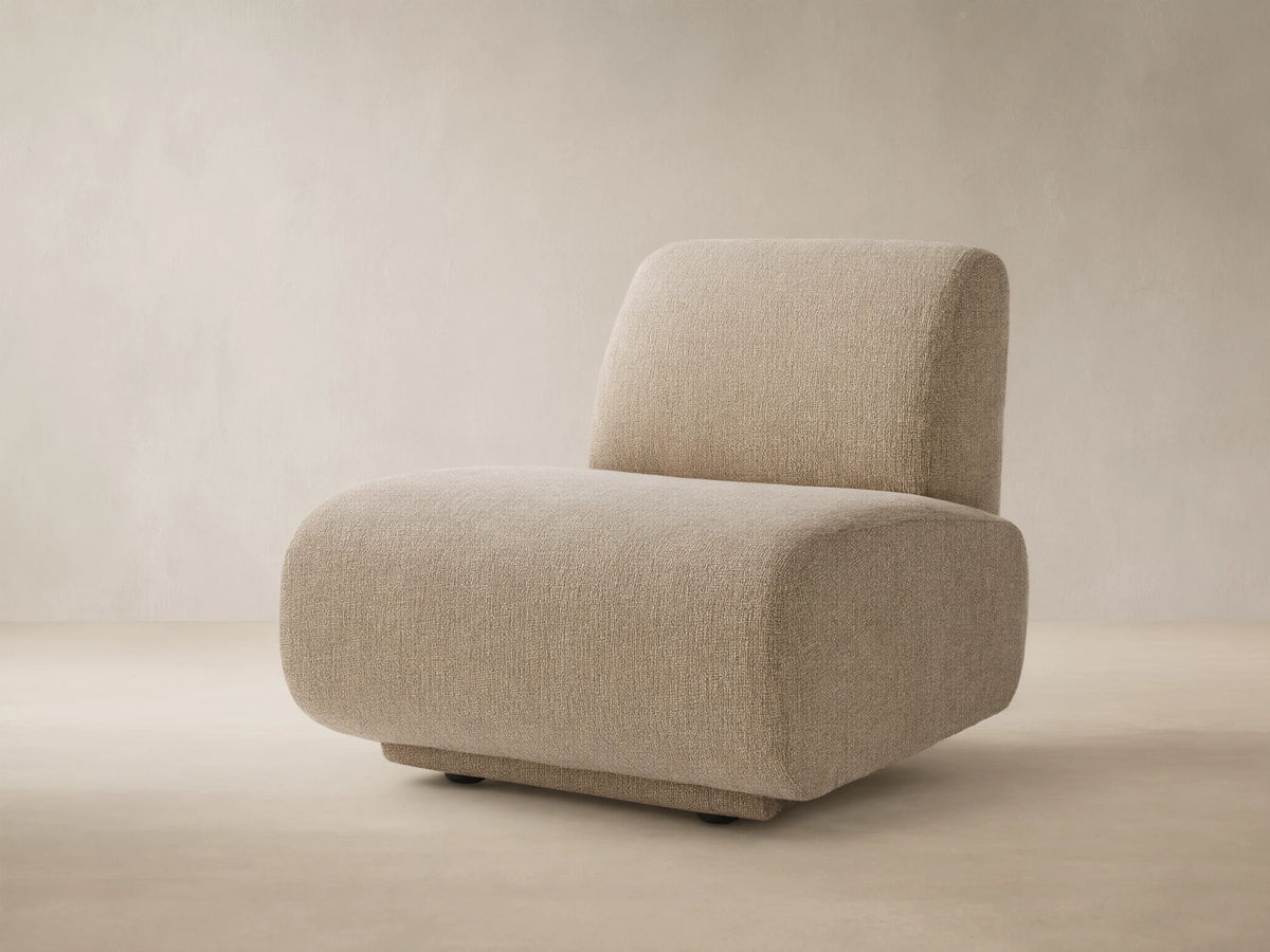 Light beige textured Gianni Outdoor Lounge Chair with rounded edges, armless, on a tiled patio floor against a warm beige wall.
