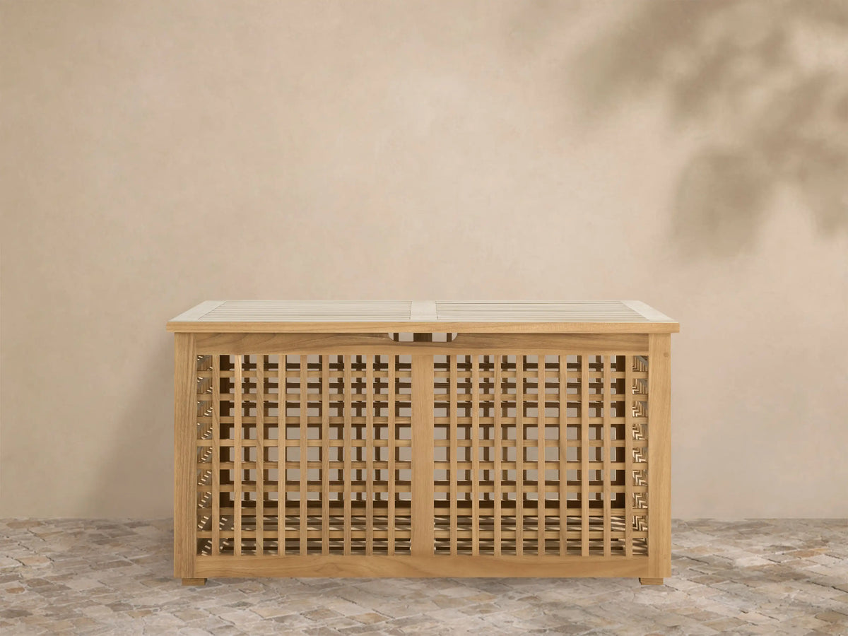 Palmeria outdoor storage box made of golden teak wood with a slatted top and intricate grid pattern on a tiled patio.