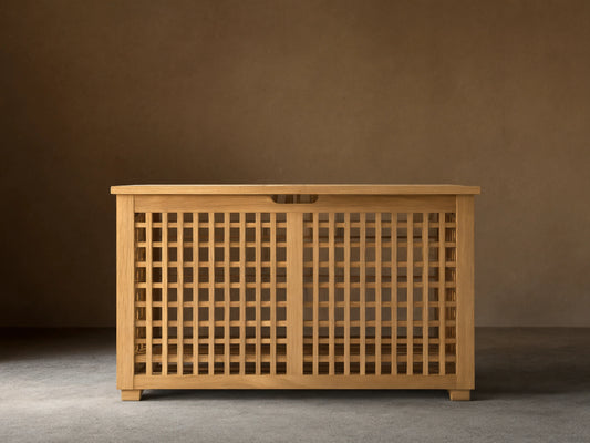 Palmeria outdoor storage box made of golden teak wood with a slatted top and intricate grid pattern on a tiled patio.