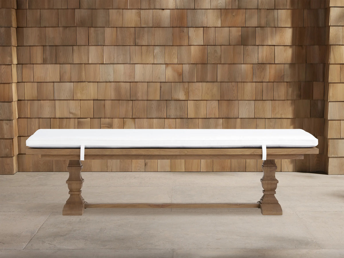 Hamptons Outdoor Dining Bench in weathered fawn teak wood with thick white cushion. Trestle style base against wood shingles.