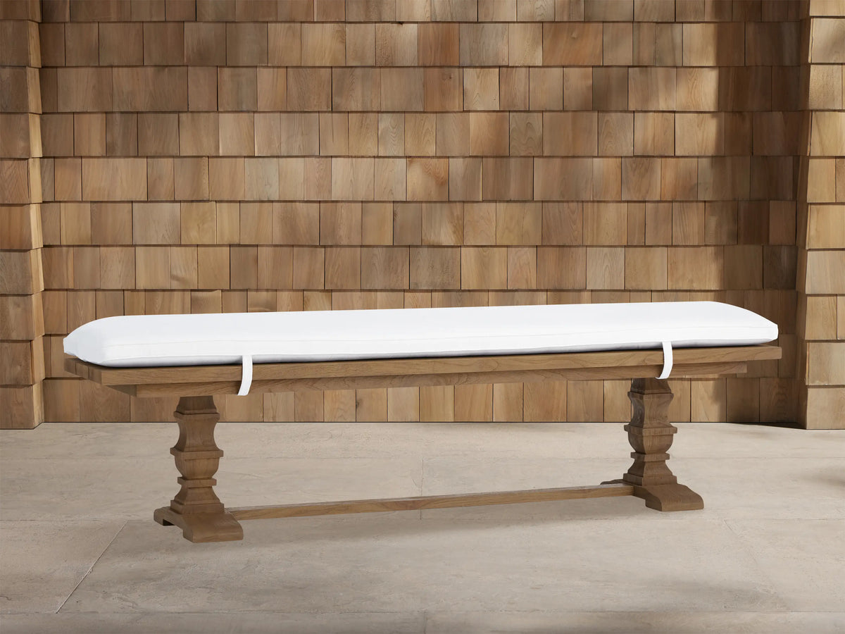 Hamptons Outdoor Dining Bench in weathered fawn teak wood with thick white cushion. Trestle style base against wood shingles.