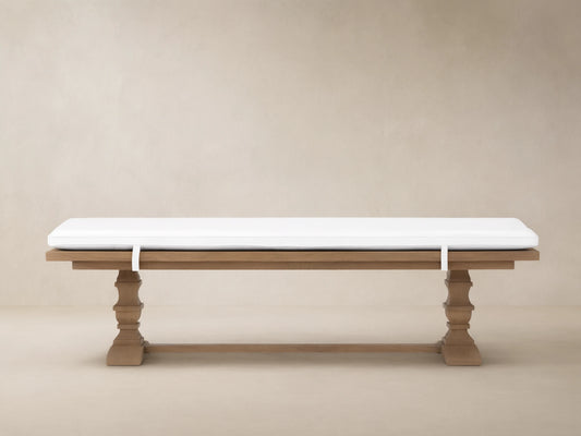 Hamptons Outdoor Dining Bench in weathered fawn teak wood with thick white cushion. Trestle style base against wood shingles.
