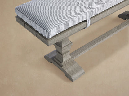 Hamptons Outdoor Dining Bench in weathered fawn, with a pinstripe blue cushion, against a wood shingle wall.