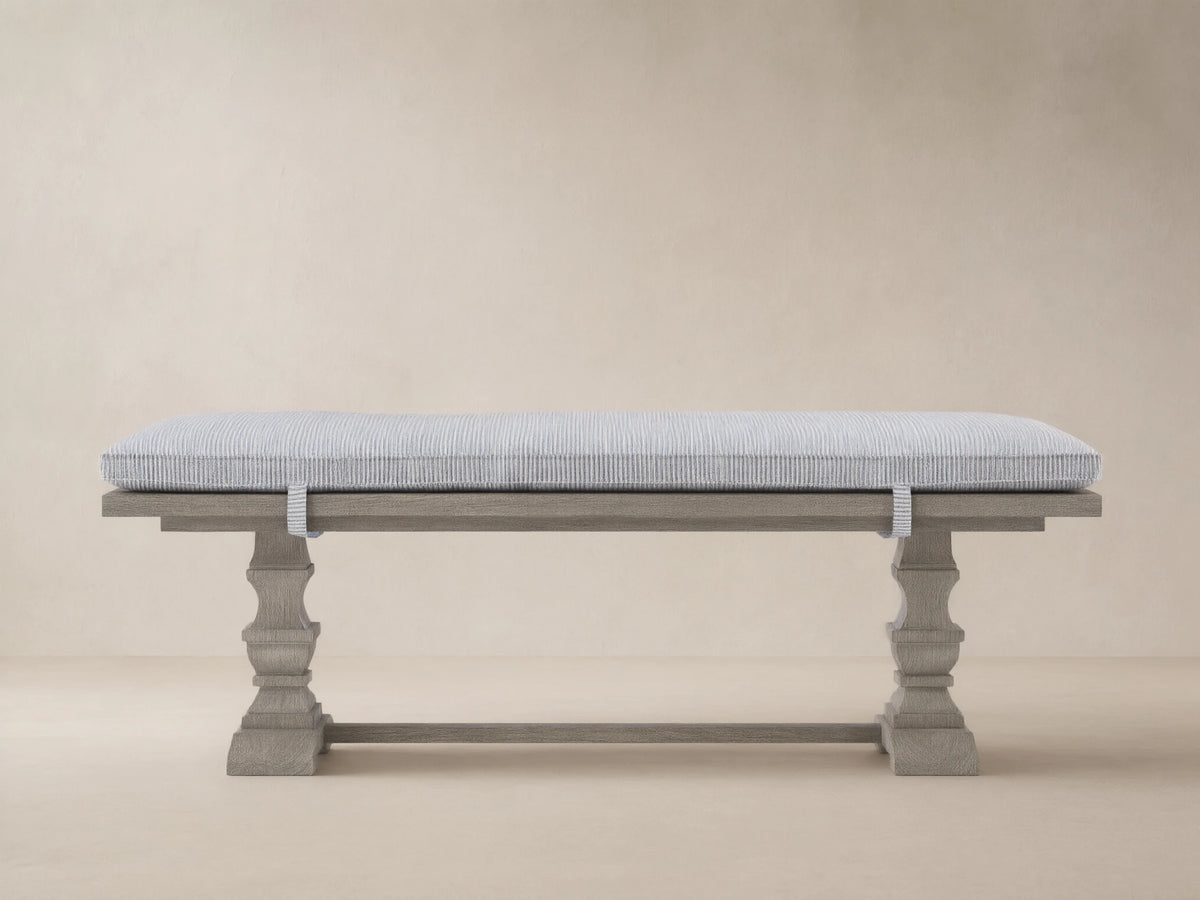 Hamptons Outdoor Dining Bench in weathered fawn, with a pinstripe blue cushion, against a wood shingle wall.