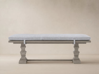 Hamptons Outdoor Dining Bench in weathered fawn, with a pinstripe blue cushion, against a wood shingle wall.