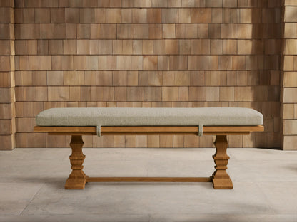 Hamptons Outdoor Dining Bench: light brown teak wood with ornate legs, long light green cushion, against a wood shingle wall.