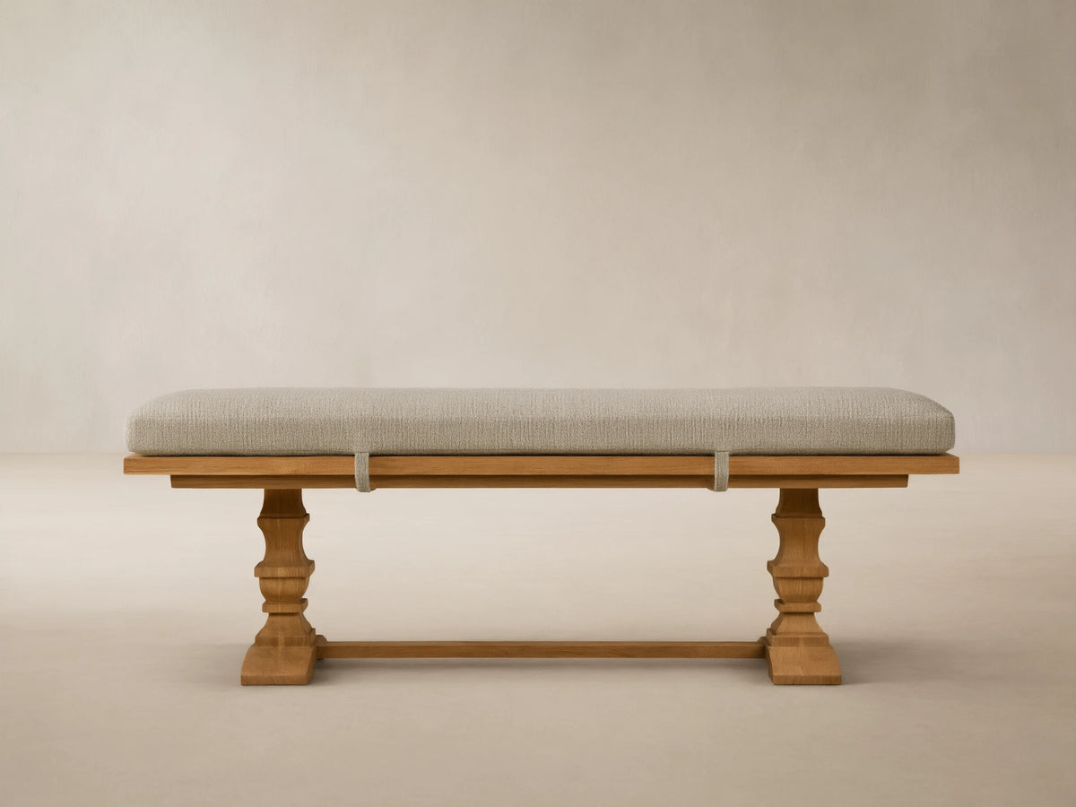 Hamptons Outdoor Dining Bench: light brown teak wood with ornate legs, long light green cushion, against a wood shingle wall.
