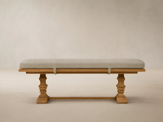 Hamptons Outdoor Dining Bench: light brown teak wood with ornate legs, long light green cushion, against a wood shingle wall.