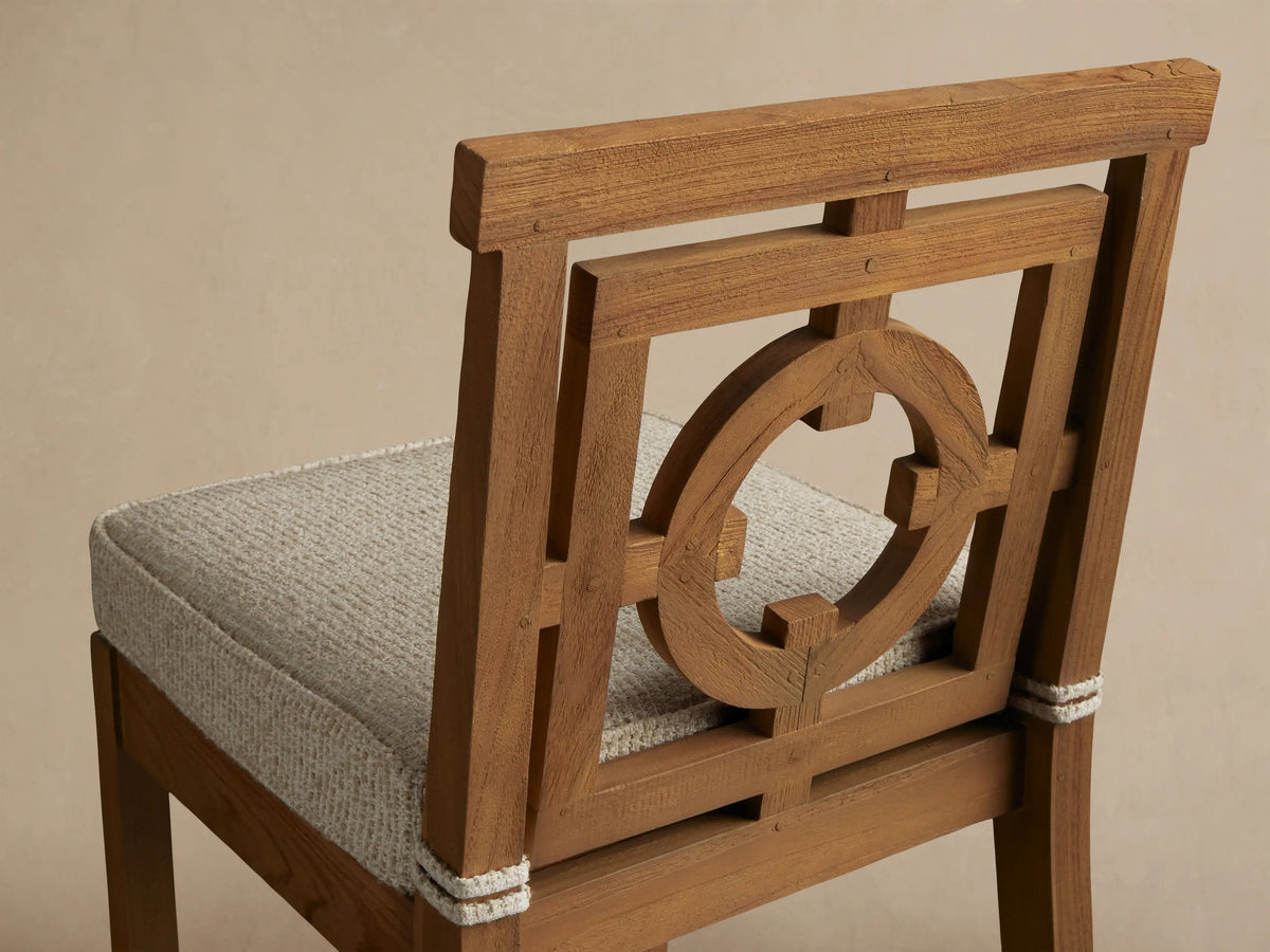 Hamptons Outdoor Barstool in weathered fawn teak. Features an ornate geometric circle pattern back, light textured cushion, on concrete floor against wood shingle wall.