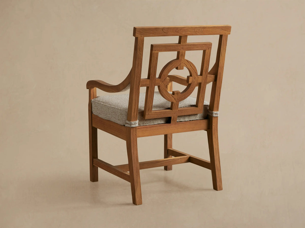 Close-up of a Hamptons Outdoor Dining Arm Chair, featuring a light brown distressed teak wood frame with geometric backrest & light woven seat.