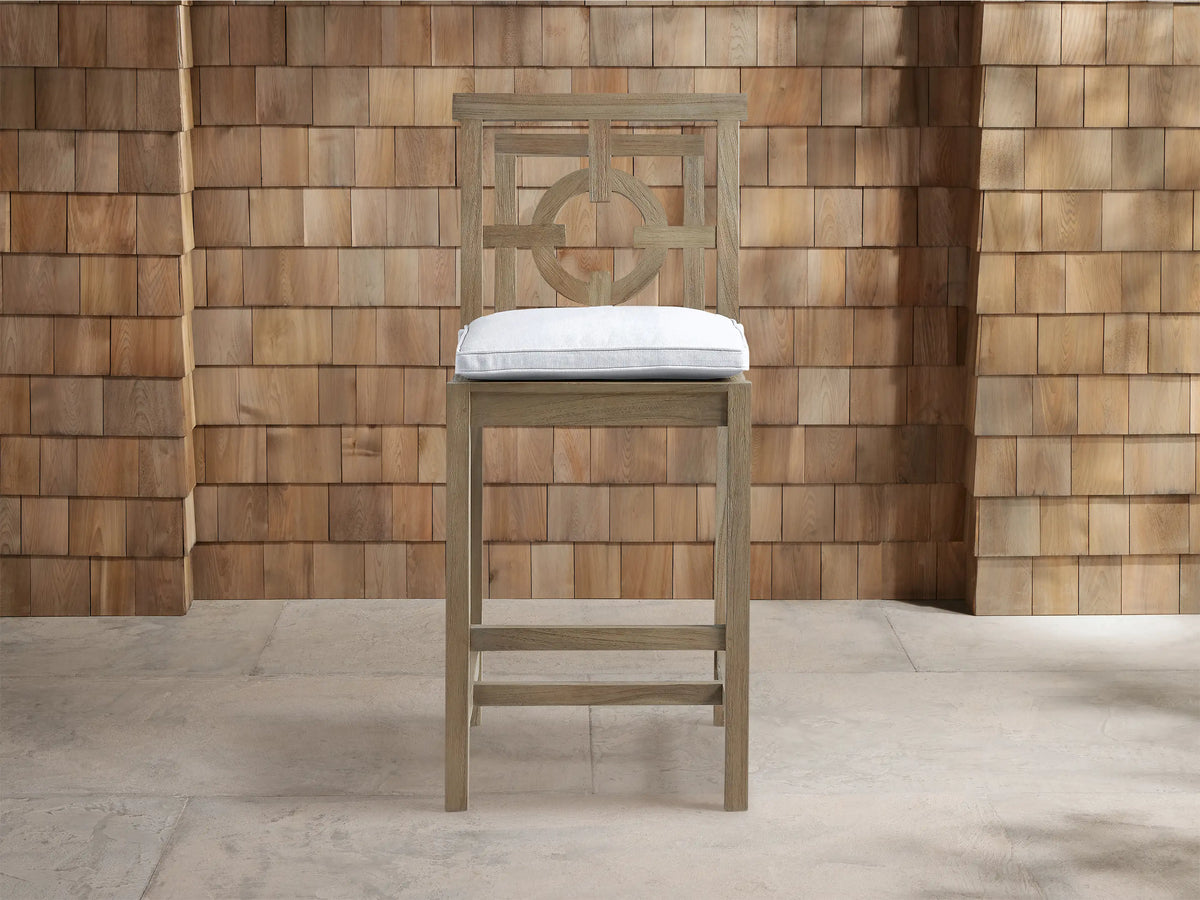 Hamptons Outdoor Barstool, weathered fawn wood, front view, light cushion, geometric circle design on back, against shingle wall.