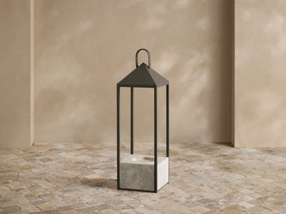 Helios Outdoor Lantern with dark bronze frame and grey marble base, featuring a glowing flameless candle on a tiled floor.