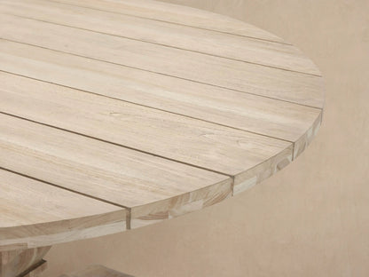 Hamptons Outdoor Round Dining Table, natural light wood with a plank top & chunky, sculpted pedestal base, on a rustic tiled floor.