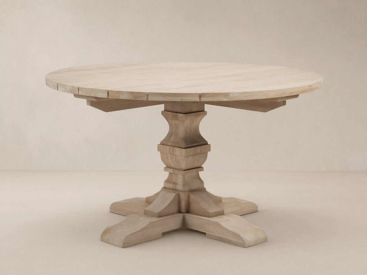 Light teak Hamptons Outdoor Round Dining Table, with carved pedestal base & splayed feet, on a patterned patio.