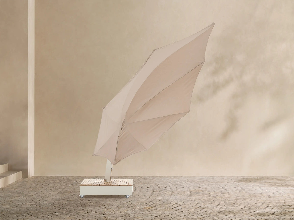 Icarus Outdoor Umbrella in Sand with an open, sand-colored canopy and curved white frame, angled over a slatted wooden wheeled base.
