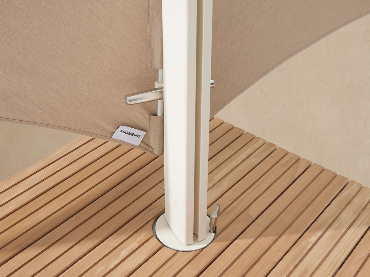 Angled Icarus Outdoor Umbrella, sand-colored canopy, white base with wood slats, on a textured stone patio.