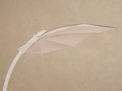 Close-up of Icarus Outdoor Umbrella in sand. Beige canopy, cream pole with silver handle, white base on slatted wood surface.