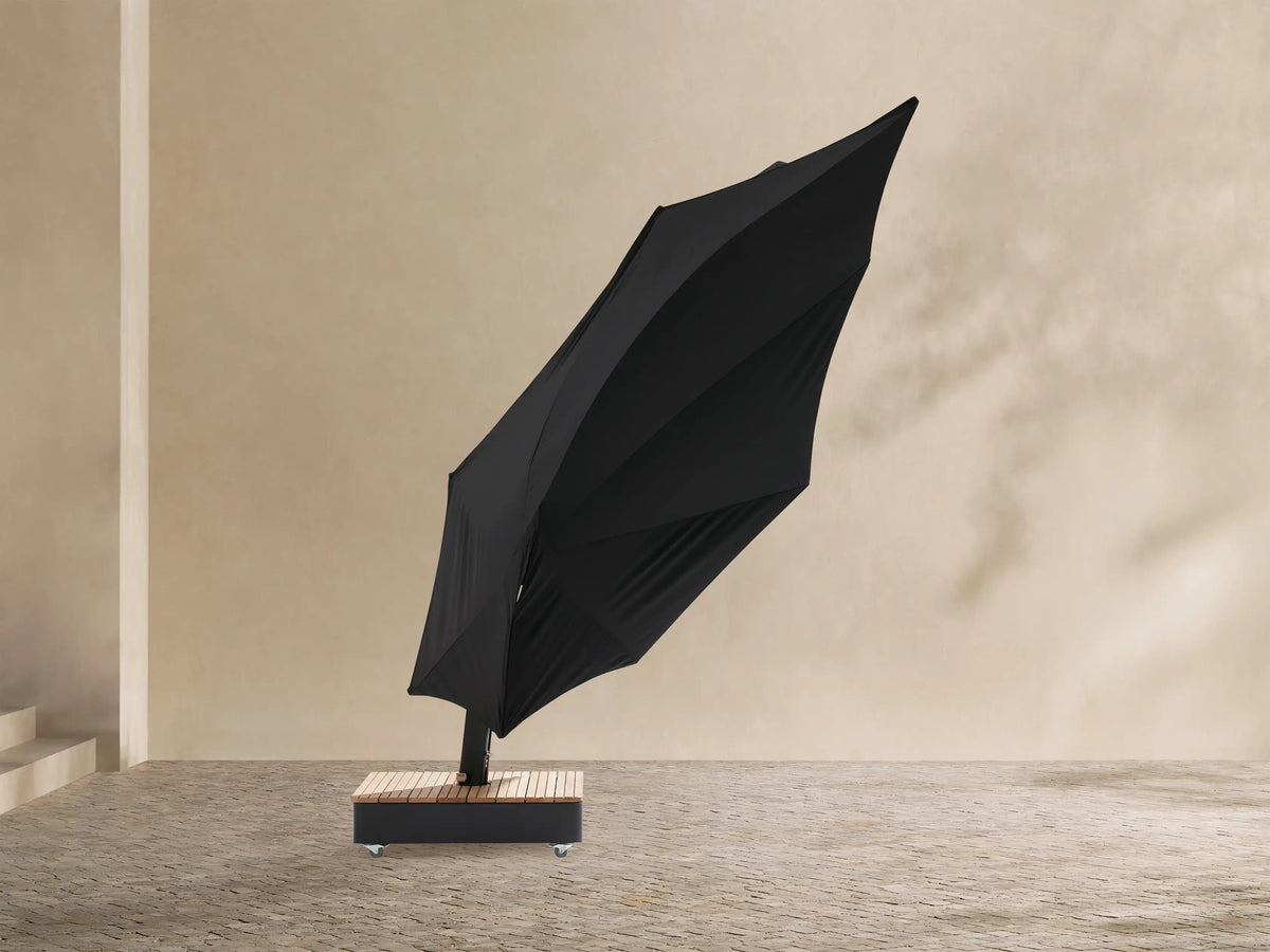 Black Icarus outdoor umbrella, open and tilted to the right, with a curved dark gray pole and a light wood-slatted base on wheels.